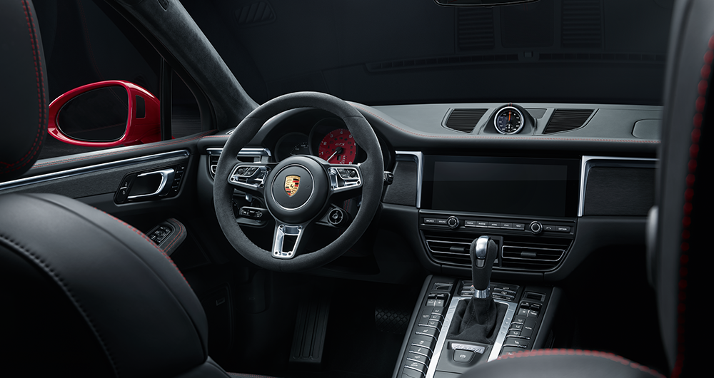 Interior del Porsche Macan GTS con volante deportivo de Alcántara, logo Porsche dorado y pantalla táctil