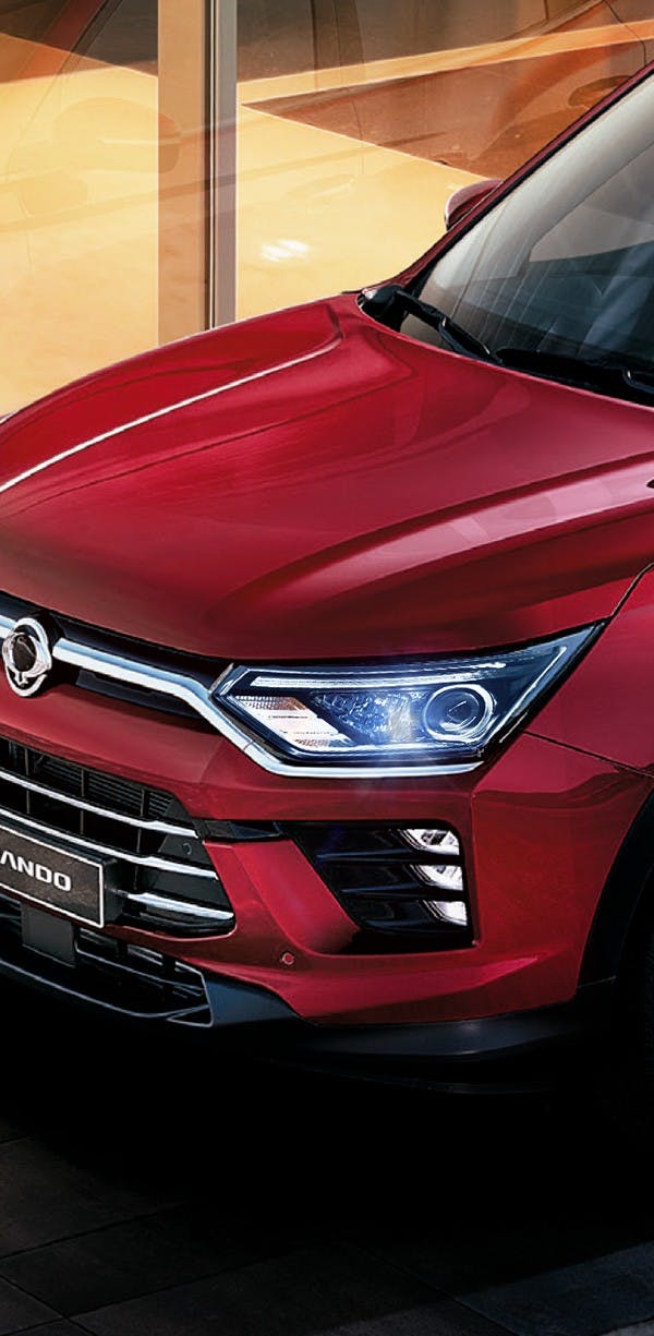 Primer plano del faro delantero LED y capó de SUV SsangYong Korando roja en showroom iluminado