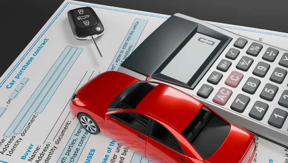 Miniatura de auto rojo sobre contrato de compra de vehículo junto a calculadora y llave de auto
