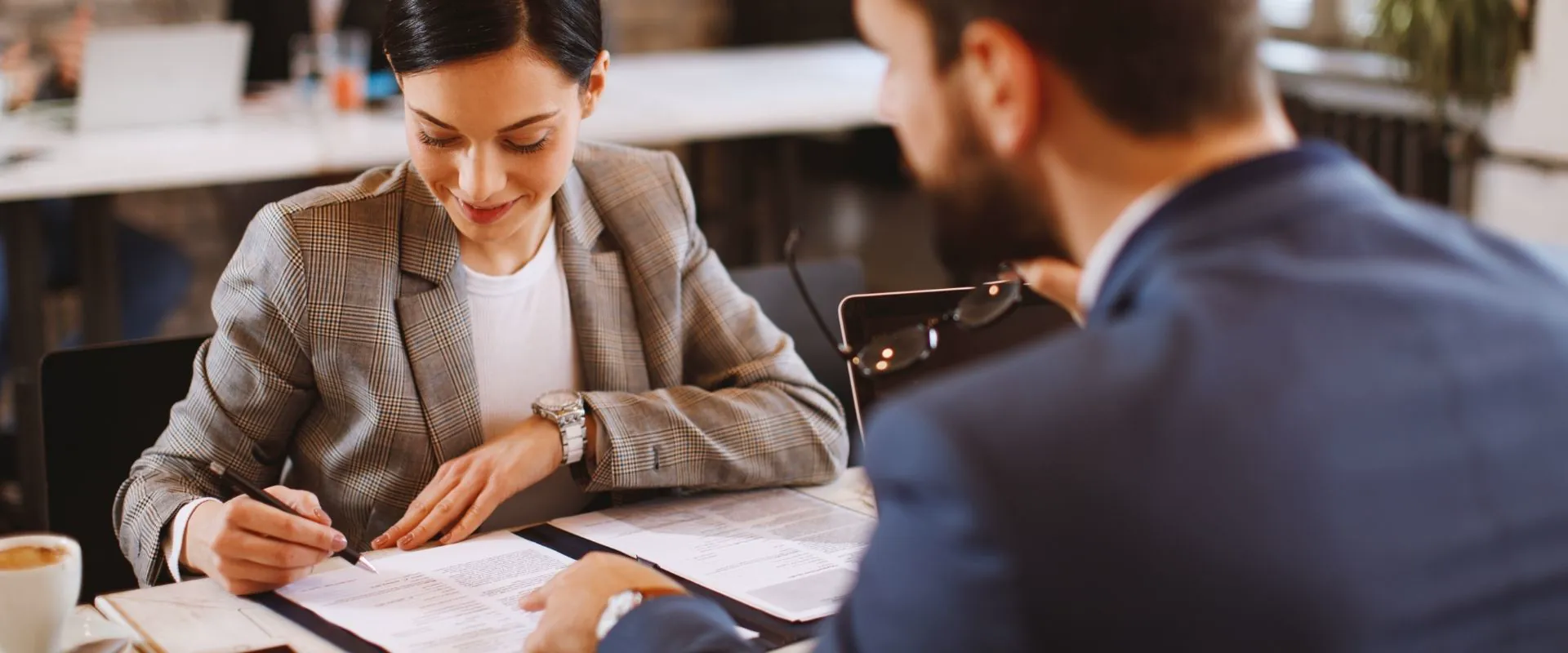 Mujer de negocios firmando un contrato frente a un colega en una oficina moderna