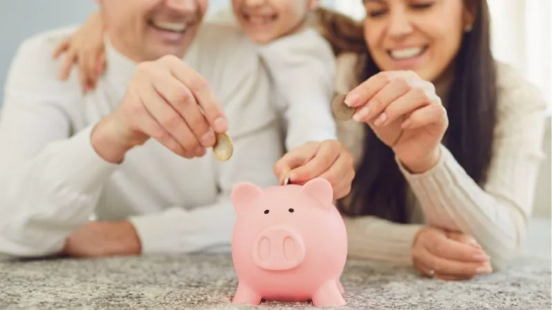 Familia feliz introduciendo monedas en una alcancía rosada sobre el suelo