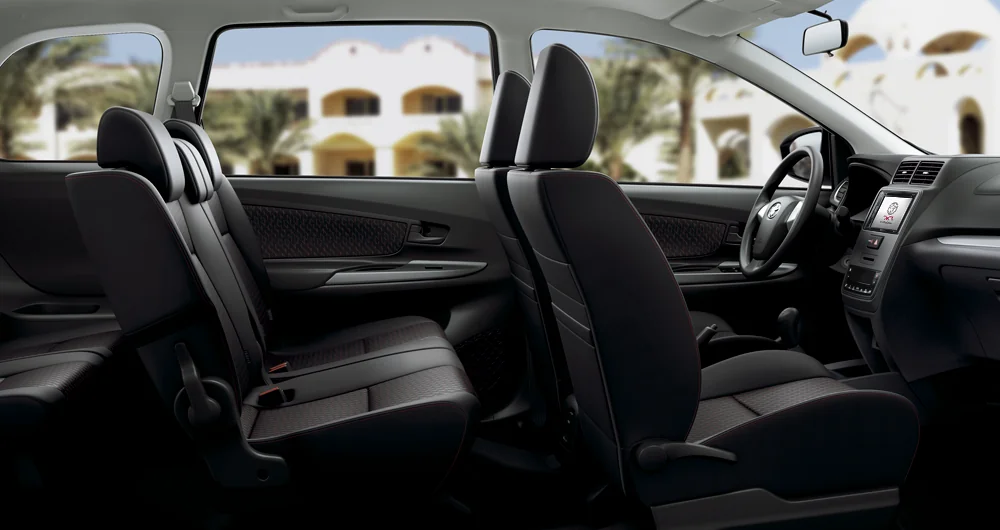 Interior Toyota con tres filas de asientos negros, tablero con pantalla táctil y palancas visibles, vista lateral completa