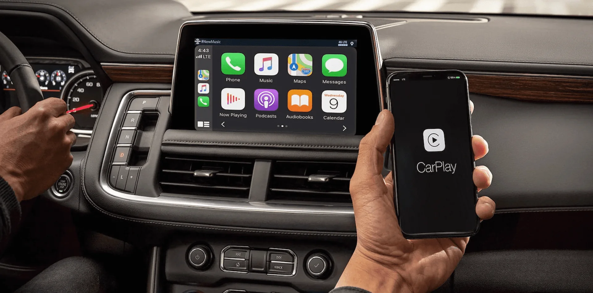 Interior del Chevrolet Suburban con pantalla táctil mostrando Apple CarPlay y mano sosteniendo un iPhone