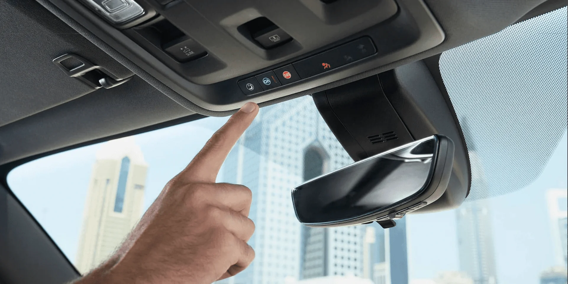 Mano señalando los botones del techo interior del Chevrolet Suburban con vista a edificios en el fondo