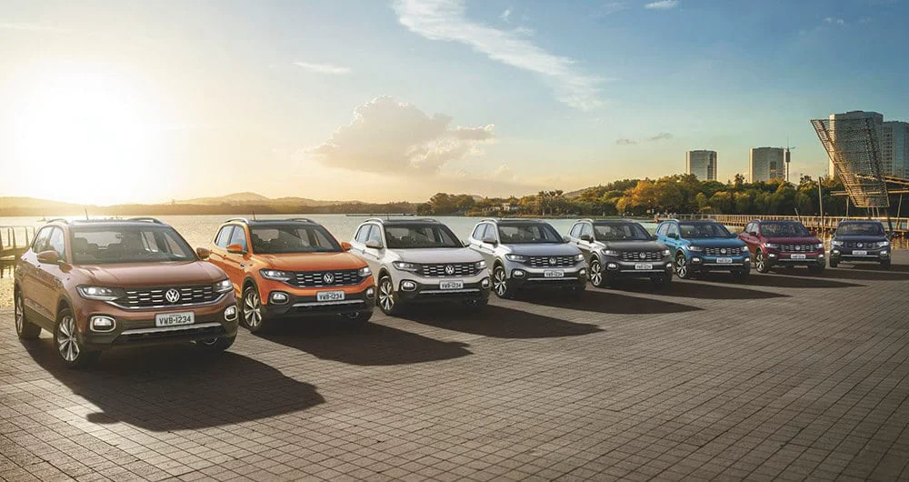 Fila de siete Volkswagen T-Cross en distintos colores estacionados frente a un lago al atardecer