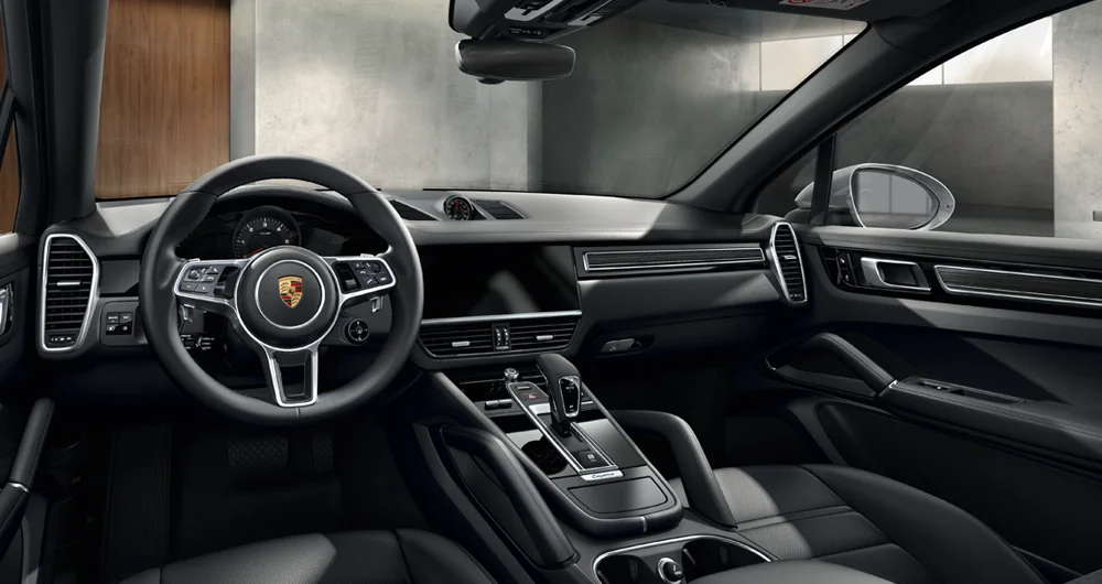 Interior del Porsche Cayenne con volante logo Porsche, pantalla central apagada y consola plateada en ambiente de showroom