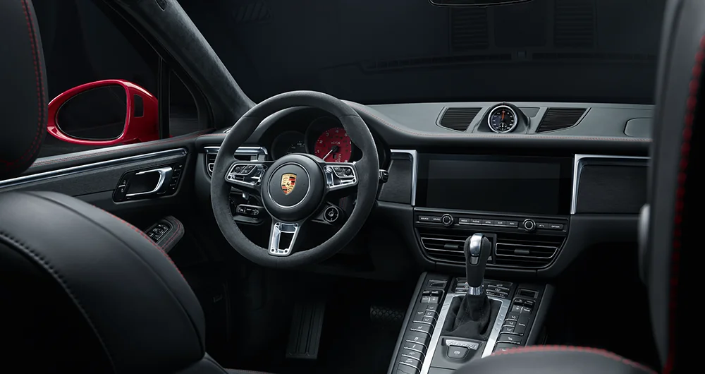 Interior del Porsche Macan GTS con volante deportivo de Alcántara, logo Porsche dorado y pantalla táctil