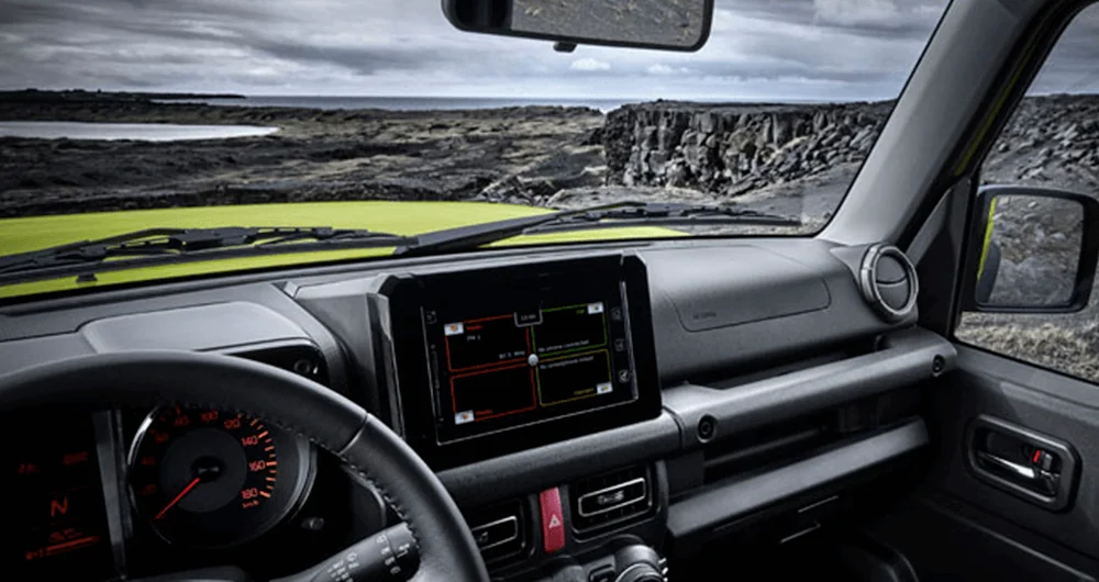 Tablero del Suzuki Jimny con pantalla táctil y paisaje rocoso al fondo a través del parabrisas