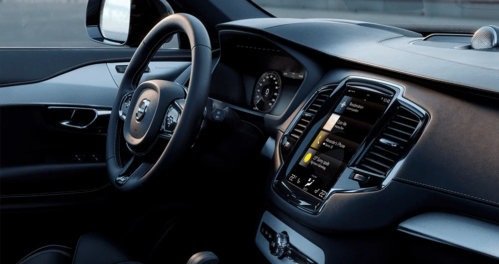 Interior Volvo XC90 vista del conductor, volante con logo Volvo y pantalla táctil vertical encendida con menú