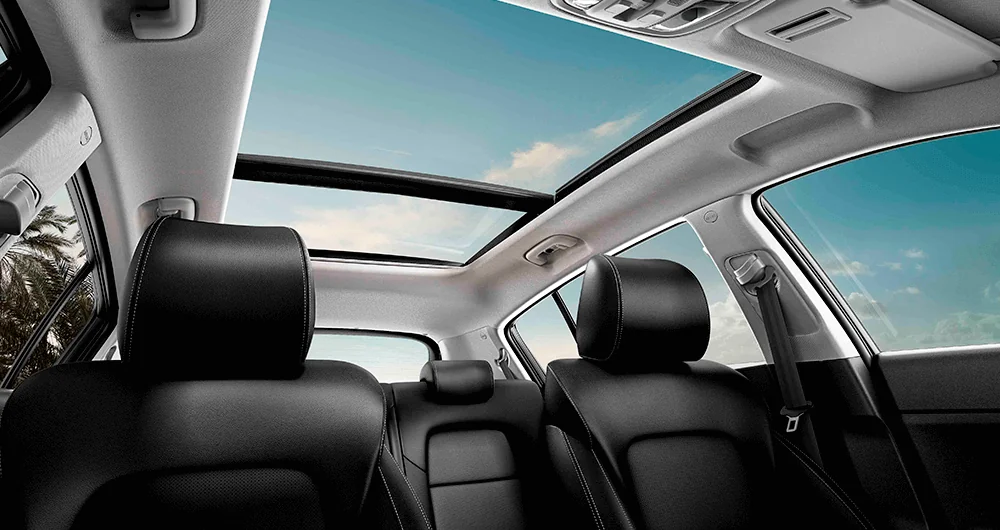 Interior del Kia Sportage con techo solar panorámico abierto y asientos traseros negros bajo cielo azul