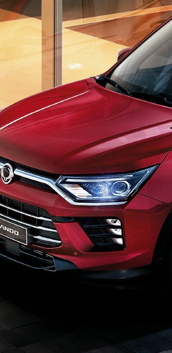 Primer plano del faro delantero LED y capó de SUV SsangYong Korando roja en showroom iluminado