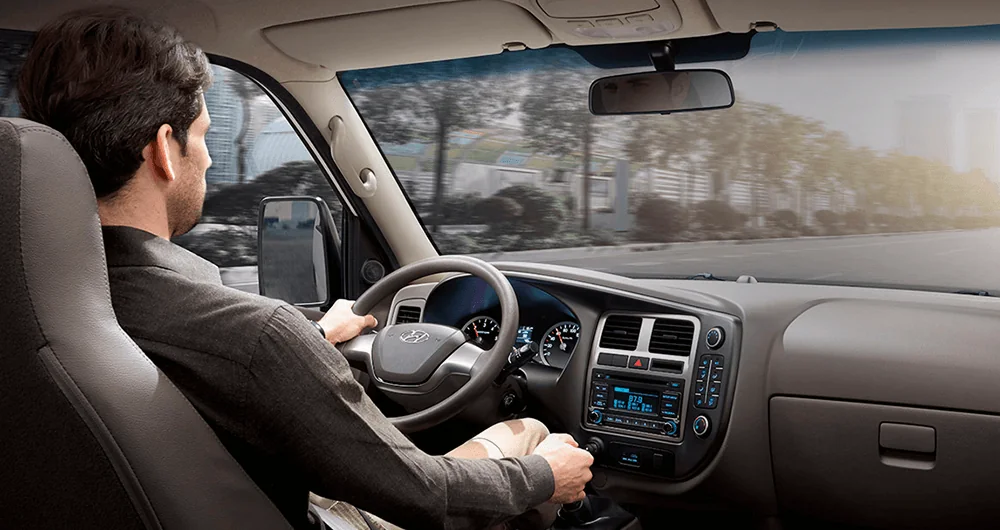 Conductor al volante del Hyundai H100 conduciendo por ciudad, vista desde el asiento del copiloto hacia el tablero