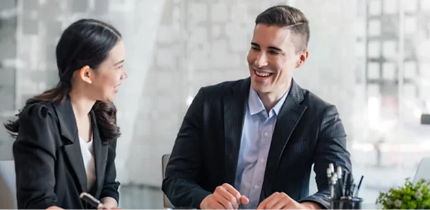 Dos profesionales sonriendo y conversando en reunión de negocios en oficina moderna
